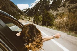 woman riding on vehicle putting her head and right arm outside the window while travelling the road by averie woodard courtesy of Unsplash.